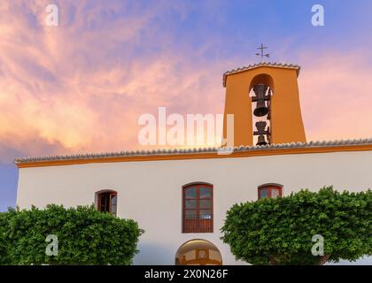 The Church of Santa Gertrude in Santa Gertrudis de Fruitera, Ibiza, gleams under sunset sky, with its distinct orange bell tower and lush greenery enh Stock Photo