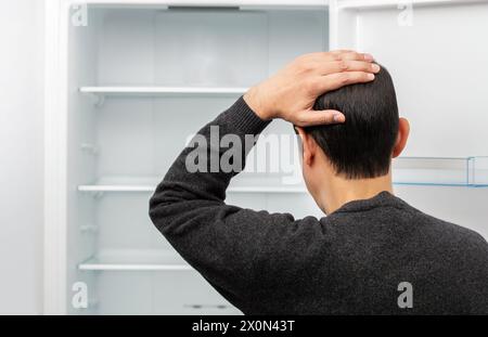 Rear view of a confused young man looking at food in refrigerator with copy space. Stock Photo