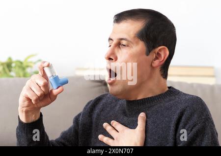 Man holding inhaler with asthma attack suffocating sitting on a couch in the living room at home Stock Photo