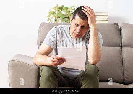 Furious man reading a letter sitting on a couch at home Stock Photo
