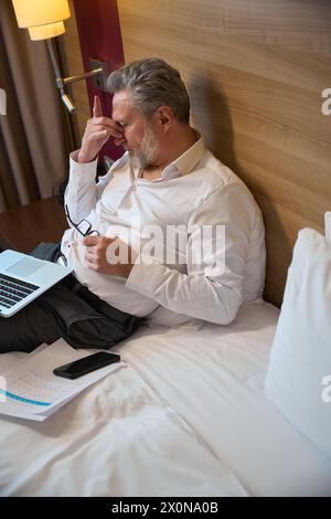 High angle view tired adult caucasian businessman during work on bed Stock Photo