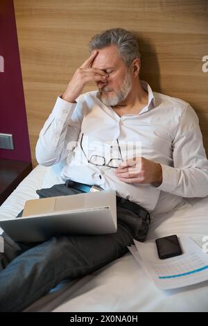 High angle view exhausted adult caucasian male entrepreneur during work on bed Stock Photo