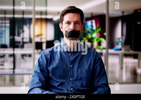 Young Man With Black Duct Tape Over His Mouth In Office Stock Photo