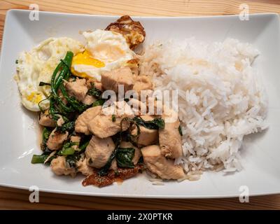 Indulge in the flavors of Thai basil chicken served with a perfectly fried egg, broccolini, and fragrant jasmine rice, elegantly presented on a white Stock Photo