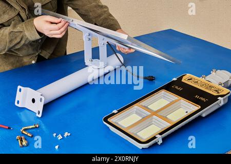 Electrician installs solar panel on mounting bracket holder for stand-alone cordless LED street light. Stock Photo
