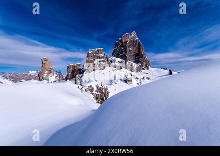 Snowdrift creating artful structures in winter, snow-covered slopes of alpine Dolomite landscape and summits of the Cinque Torri group in the distance Stock Photo