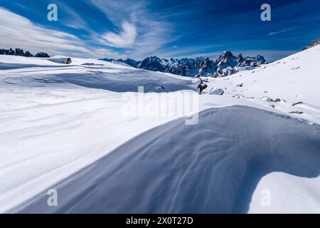 Snowdrift creating artful structures in Tre Cime Natural Park in winter, the summits of Cadini di Misurina in the distance, seen from Forcella Lavared Stock Photo