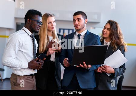 Multiethnic corporate team engage in project discussion. African, Caucasian, Arabic execs collaborate using tech. Woman, men analyze data in modern Stock Photo