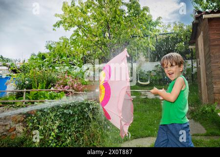 Boys enjoy water fight in garden hiding behind pink umbrella Stock Photo
