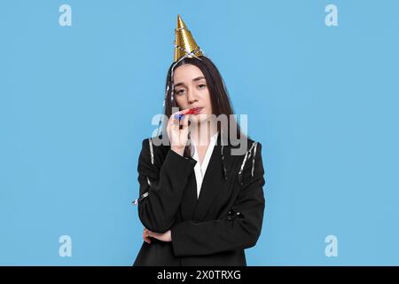 Sad woman in party hat with blower on light blue background Stock Photo