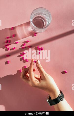 Female hand holding pink tablet on pastel background, women healthcare concept, natural light Stock Photo