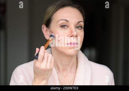 Blonde woman applying makeup with a brush at home Stock Photo