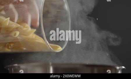 dry penne rigate poured in saucepan with boling water, wide photo Stock Photo