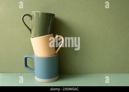 Stack of ceramic mug cups on green table. khaki wall background Stock Photo