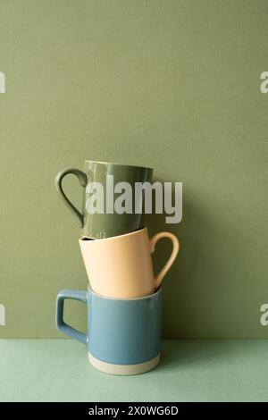 Stack of ceramic mug cups on green table. khaki wall background Stock Photo