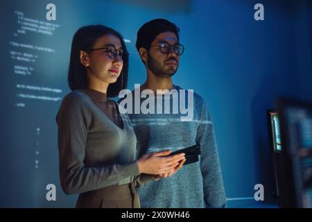 two asian and indian developer presentation about coding software data with devops team at night in office Stock Photo