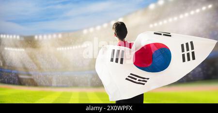 South Korea football supporter on stadium. Korean fans on soccer pitch watching team play. Group of supporters with flag and national jersey cheering Stock Photo