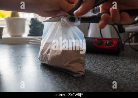 Child hands cutting plastic bag with cupcake mix powder to a mixer bowl to make a dessert dough. Stock Photo