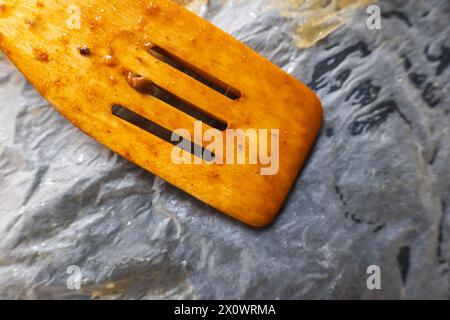 Used dirty wooden mixing spoon inside empty tray lined with baking paper. Stock Photo