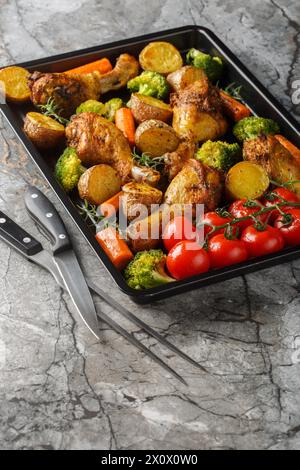 Homemade baked chicken drumsticks with vegetables and rosemary close-up on a baking sheet on the table. Vertical Stock Photo