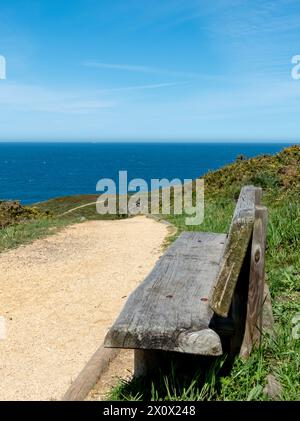 Wooden bench standing on the hiking trail near Luanco, Asturias,Spain. Beautiful spring coastal landscape. View above the sea. Stock Photo