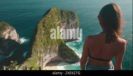 A woman stands on top of a cliff, gazing out at the vast ocean at Kelingking Secret Point Beach on Nusa Penida Island, Indonesia. Stock Photo
