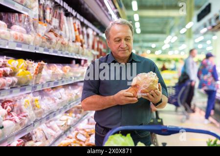 Elderly man chooses chicken meat in supermarket Stock Photo