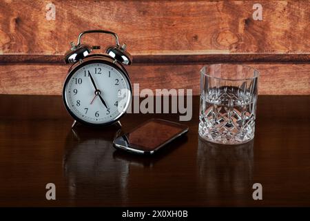 Alarm clock with glass of water and mobile phone on a wooden bedside shelf Stock Photo