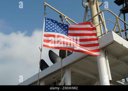 Flying American flag on the wind hanging on the navigational mast near exhaust pipes of funnel on the merchant container vessel. Stock Photo