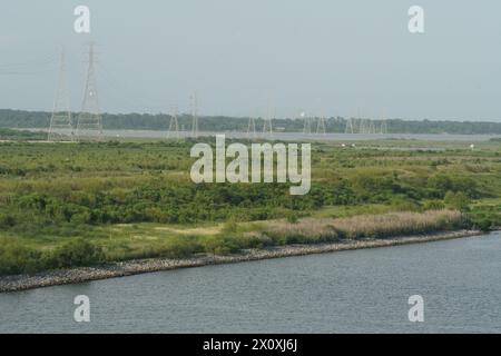 High electric pylons partly on a green field and partly passing through the water observed from the container terminal of the Port of Houston. Stock Photo