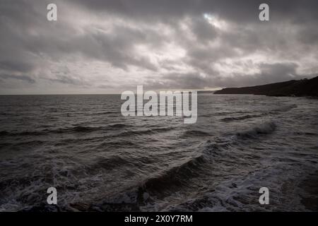 Waves roll onto a beach under stormy skies with a dark coastline in the distance, Scarborough, North Yorkshire, England. Stock Photo