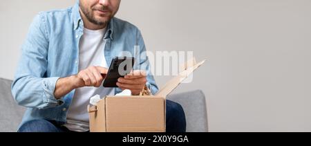 Man in a denim shirt parcel a package and takes a photo of his purchase, internet order. Person sharing feedback with online store using his smartphon Stock Photo