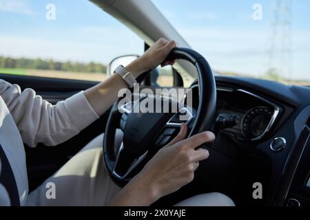 Inside view of woman driving car on countryside road. Female drivers hands on steering wheel Stock Photo