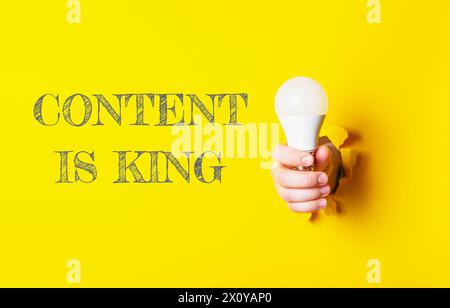 A person holding a light bulb with the words content is king written behind them. The image conveys the idea that content is king, emphasizing the imp Stock Photo