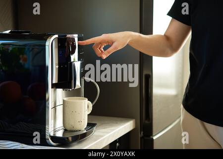 Woman preparing fresh cup of coffee with modern espresso machine. Female hand pressing button on coffee machine Stock Photo