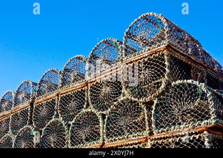 Close up of creels, crab pots or lobster pots stacked up on the quayside of Arbroath harbour during the winter, isolated against a clear blue sky. Stock Photo
