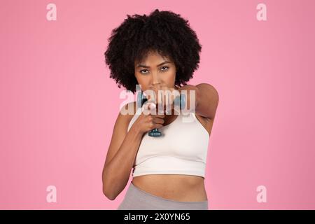 Focused woman doing bicep curls on pink background Stock Photo