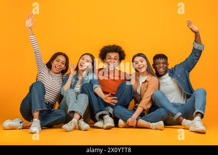 Friends sitting and raising hands joyfully on orange background Stock Photo
