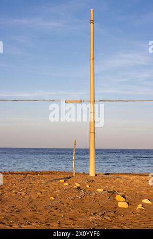 In the time of sunrise, sand on the beach colored into golden. Mediterranean sea. Blue sky with light clouds. Electricity column with a horizontal cab Stock Photo