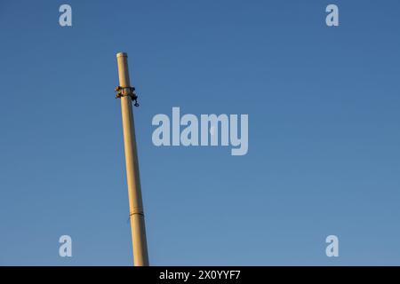 Column in the morning sunlight, colored into golden. No lamp or cable, just the pole. Bright blue sky in the background, with a moon in a half. Marsal Stock Photo