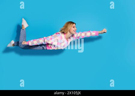 Full length photo of lovely girl wear colorful pullover flying look at sale empty space clenching fist isolated on blue color background Stock Photo