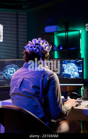 Software technician with EEG headset on programming brain transfer into computer virtual world, merging with artificial intelligence. IT expert using neuroscience to gain digital soul Stock Photo
