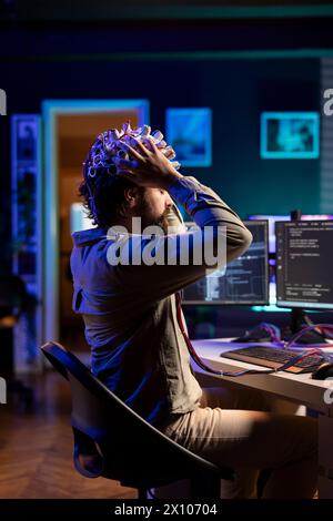 Software engineer puts EEG headset on, starting mind upload process, trying to gain bionic powers. IT admin using high tech neuroscientific gear to transfer consciousness into cyberspace Stock Photo