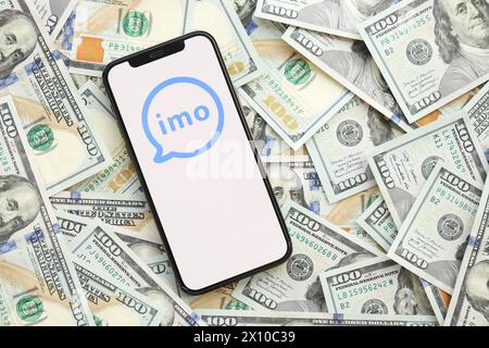 KYIV, UKRAINE - APRIL 1, 2024 Imo messenger icon on smartphone screen and many usd money bills. iPhone display with app logo and lot of hundred dollars banknotes close up Stock Photo