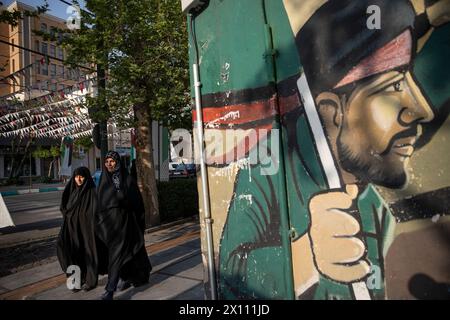 Tehran, Tehran, Iran. 14th Apr, 2024. two women walk past a mural in Felestin (Palestine) Square, Tehran, Iran, on Sunday, April 14, 2024. Israel on Sunday hailed its air defenses in the face of an unprecedented attack by Iran, saying the systems thwarted 99% of the more than 300 drones and missiles launched toward its territory. (Credit Image: © Sobhan Farajvan/Pacific Press via ZUMA Press Wire) EDITORIAL USAGE ONLY! Not for Commercial USAGE! Stock Photo