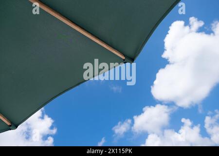 A green umbrella is open on a sunny day. The sky is clear and blue, with a few clouds scattered throughout. Scene is cheerful and relaxed, as the umbr Stock Photo