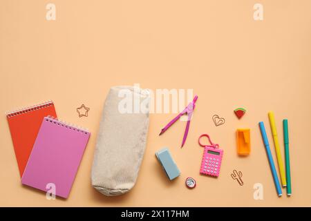 Beige pencil case with different school stationery and notebooks on orange background Stock Photo