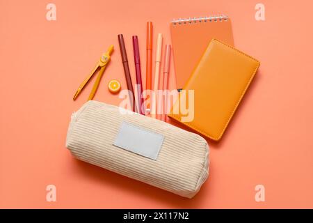 Beige pencil case with different school stationery and notebooks on orange background Stock Photo