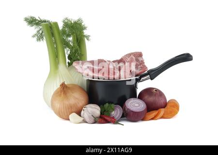 Black saucepan with pieces of raw pork atop. Around the saucepan are sliced vegetables which include onions, carrots, and garlic isolated on white bac Stock Photo