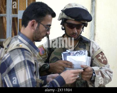 A soldier from 5th Battalion, 20th Infantry Regiment, 3rd Brigade, 2nd Infantry Division (Stryker Brigade Combat Team) and an interpreter review identification papers of a resident while multinational forces search his house in Qabr Abd, a city south of Mosul, during Operation Mayfield III, a cordon and search operation conducted on July 19 2004. Stock Photo